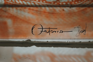 An abstract art piece featuring a mix of orange and white tones with a signature at the bottom. The upper section displays swirling patterns, while the lower section is more subdued, featuring rough textures.