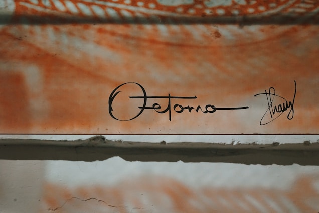 An abstract art piece featuring a mix of orange and white tones with a signature at the bottom. The upper section displays swirling patterns, while the lower section is more subdued, featuring rough textures.