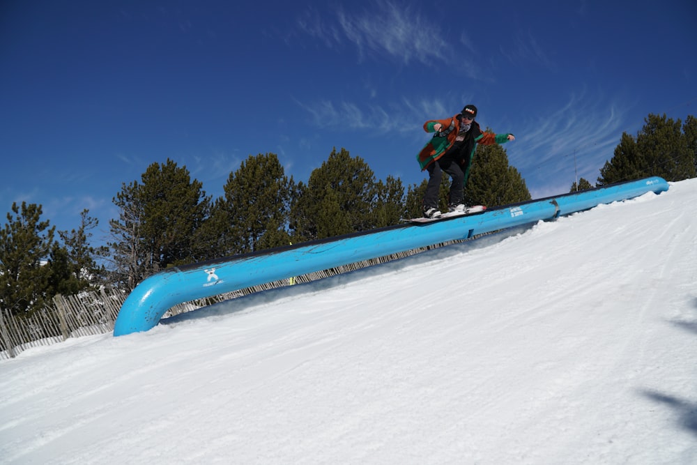 Mann in schwarzer Jacke und schwarzer Hose fährt tagsüber blaues Snowboard