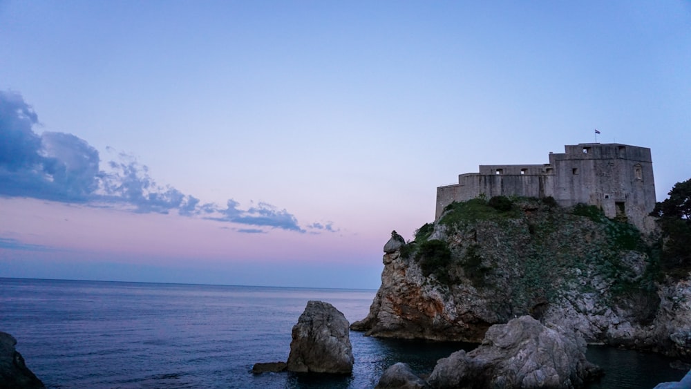 gray concrete building on cliff by the sea under blue sky during daytime