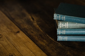 A stack of vintage books with blue-green covers is placed on a rustic, wooden surface. The books appear slightly worn, adding to their antique aesthetic.