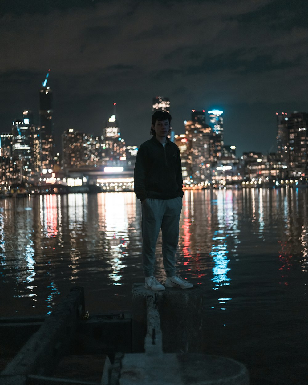 uomo in giacca nera in piedi sul molo durante la notte