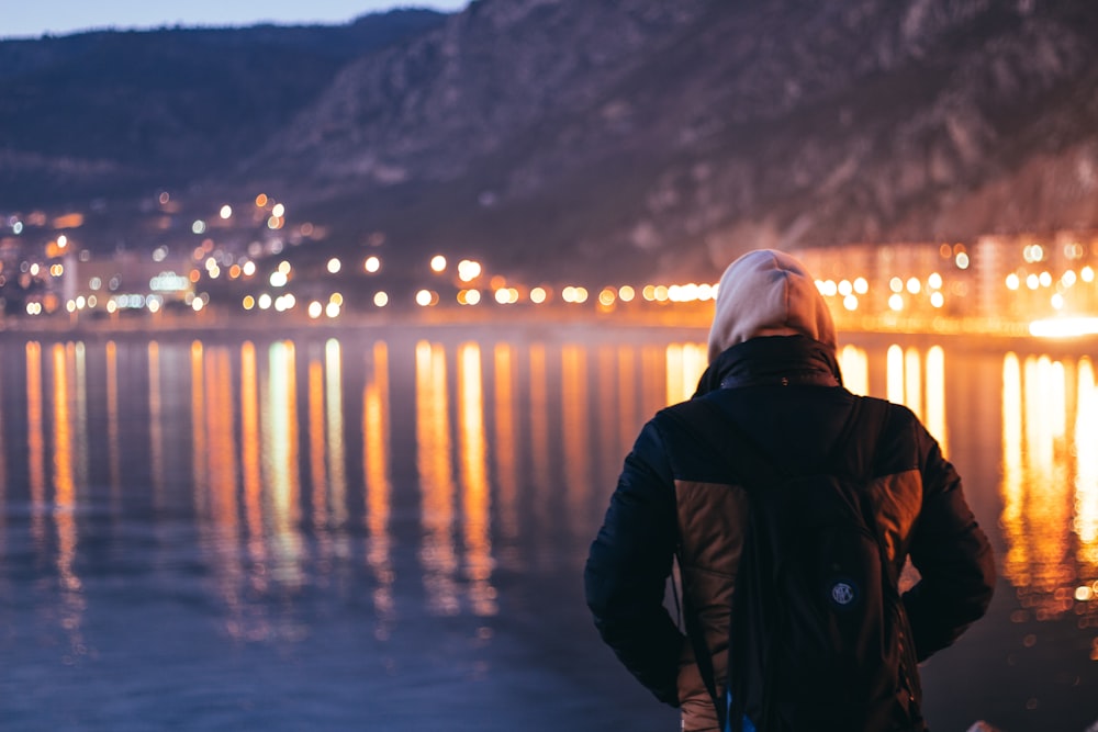 person in black jacket and white knit cap standing on seashore during night time