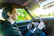 Young man happily driving a shiny rental car on a sunny day.