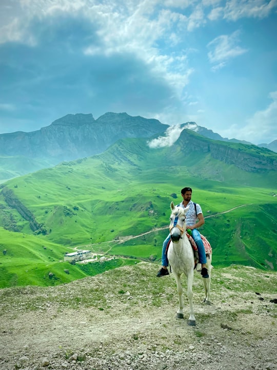 woman in white long sleeve shirt riding white horse on green grass field during daytime in Laza Azerbaijan