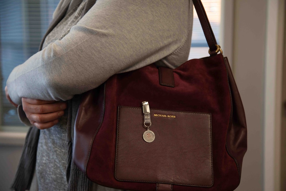 person in gray jacket holding brown leather sling bag