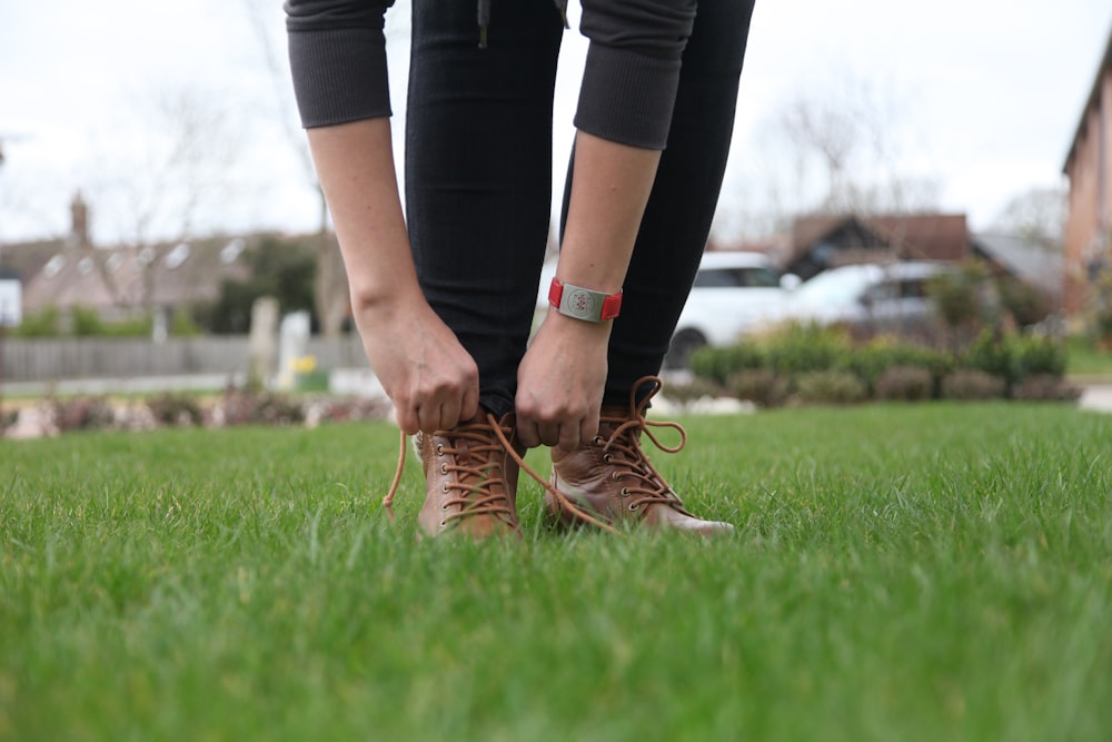 person in black leggings and brown leather shoes standing on green grass field during daytime