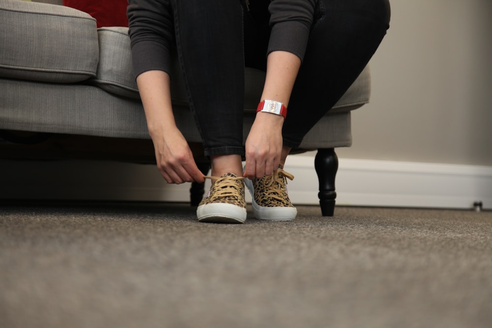 woman in black pants and white and brown shoes sitting on black and red couch