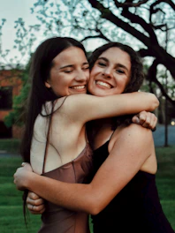 A group of diverse women smiling and embracing each other in a warm outdoor setting.