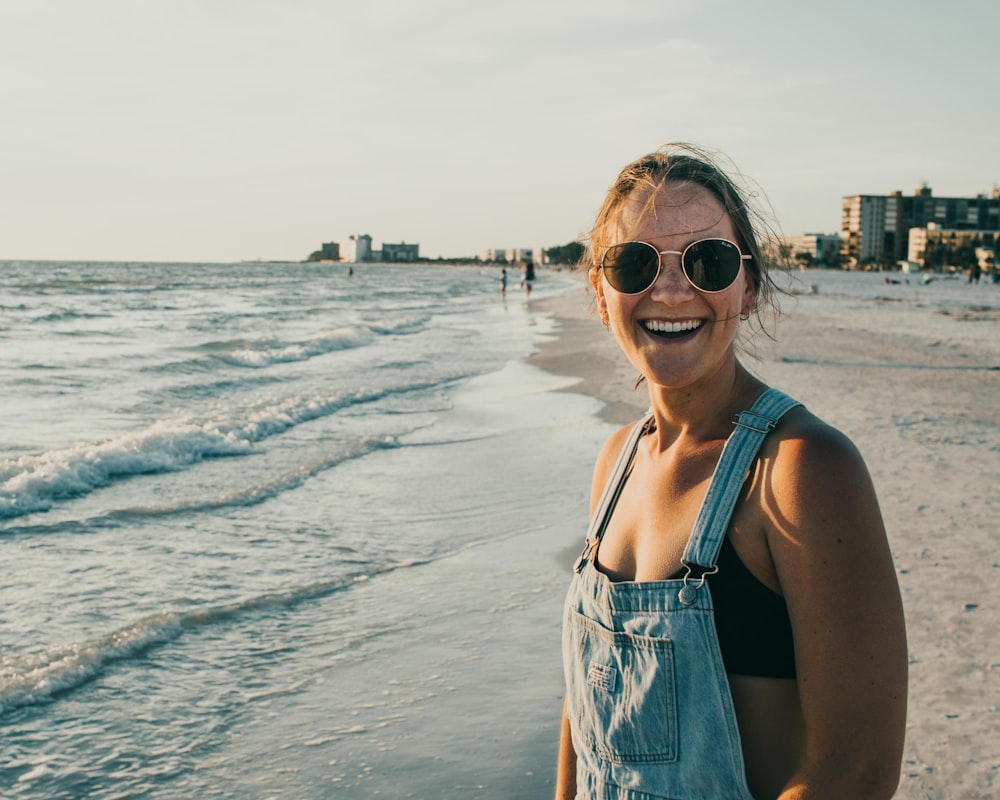 woman in blue tank top wearing sunglasses standing on beach during daytime