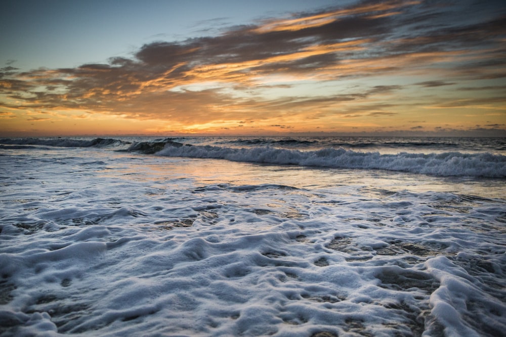 ocean waves crashing on shore during sunset