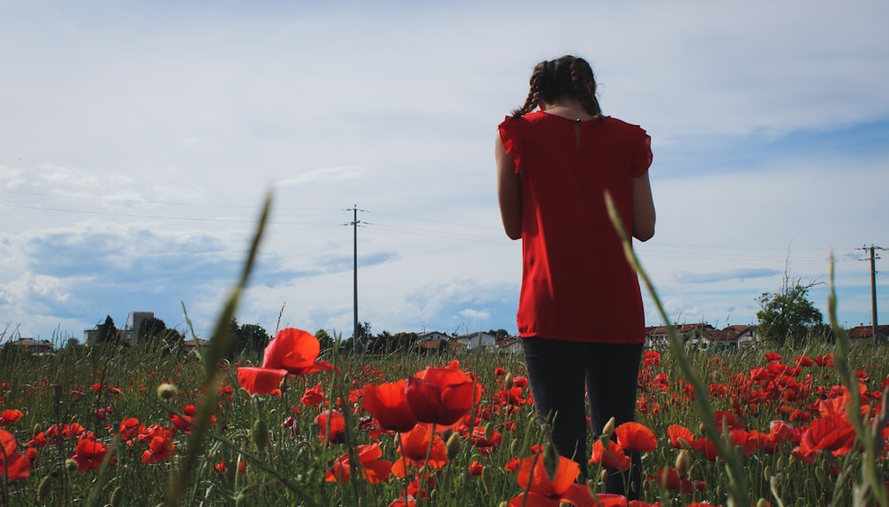 woman in red long sleeve shirt standing on red flower field during daytime