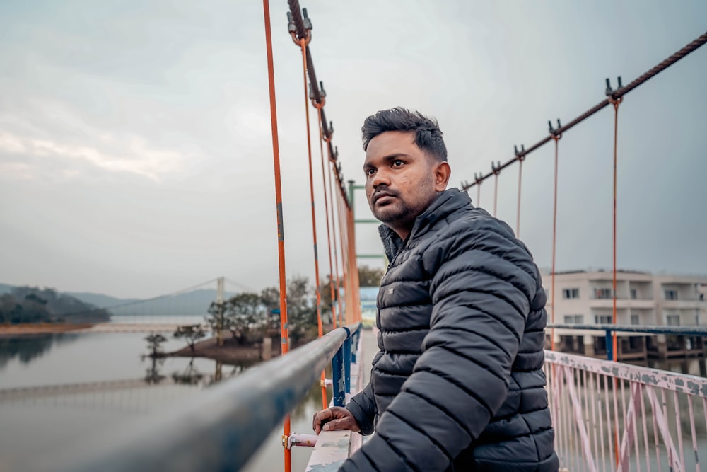 man in black and gray striped hoodie jacket standing on bridge during daytime