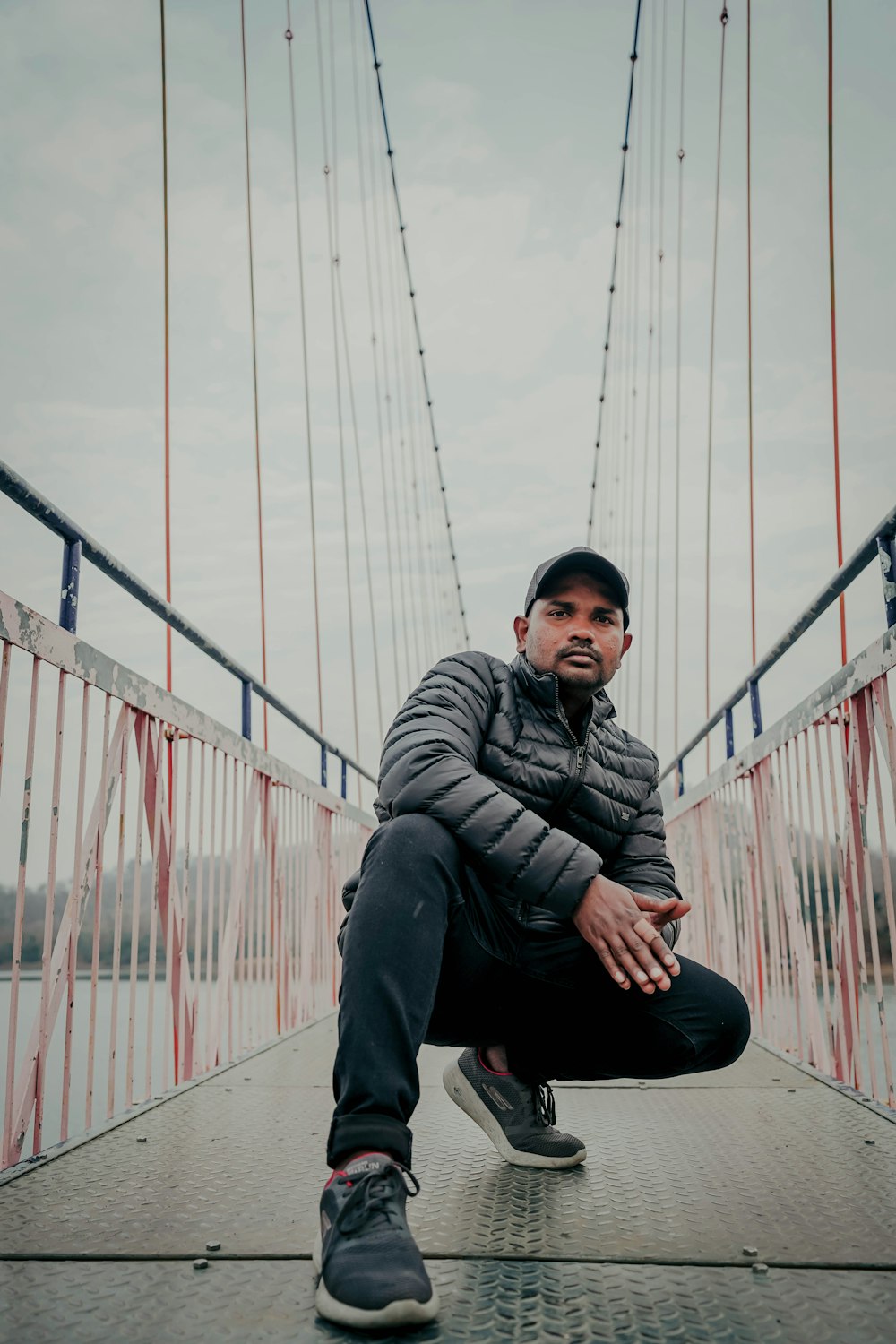 man in black jacket sitting on bridge during daytime