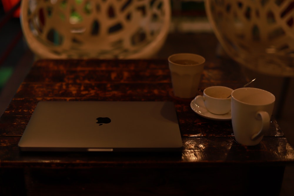 silver macbook beside white ceramic mug on brown wooden table