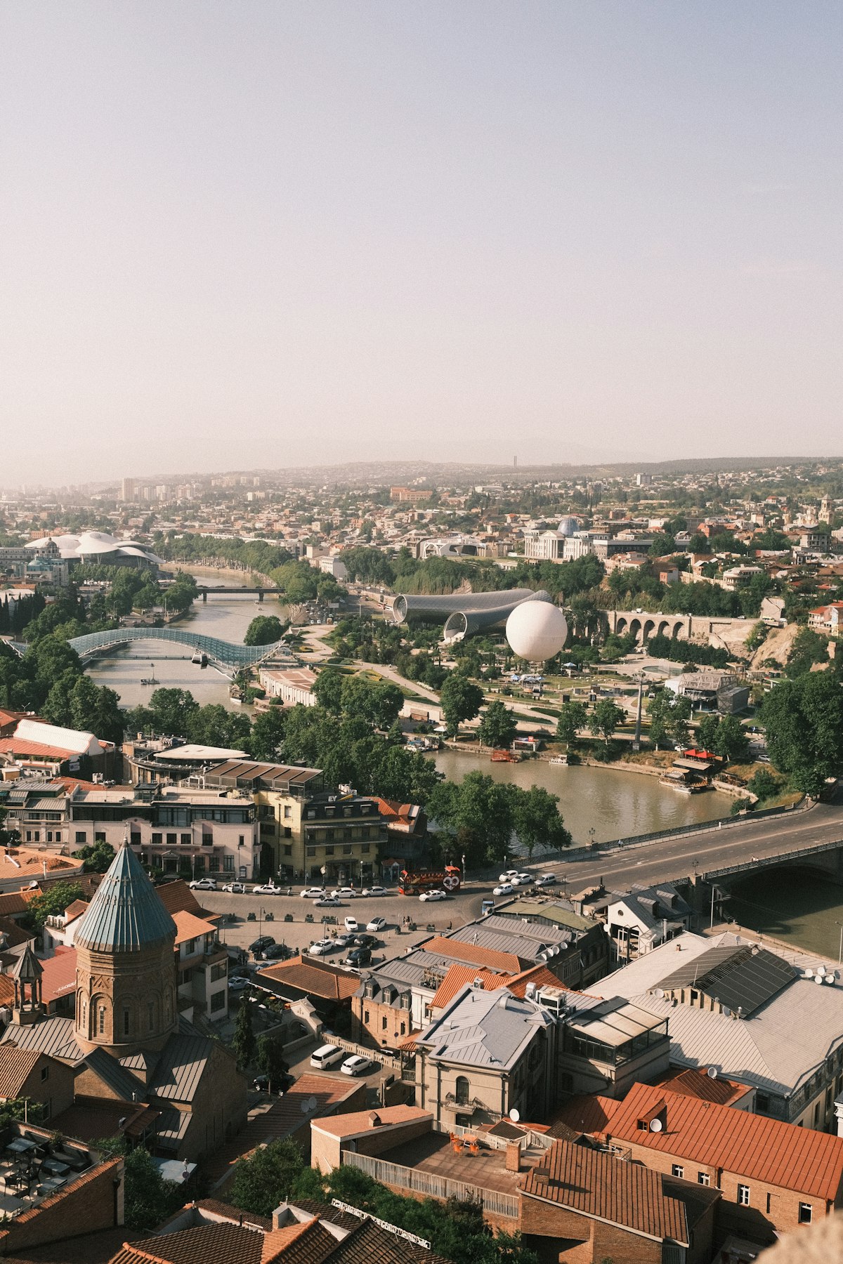 Tbilisi May — aerial view of the city with the Mtkvari River, Sameba Cathedral, and the Caucasus foothills in spring