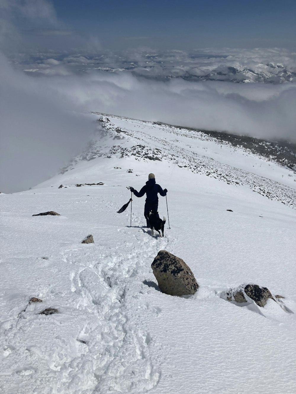 persona in giacca nera e pantaloni neri che cammina su terreno coperto di neve durante il giorno