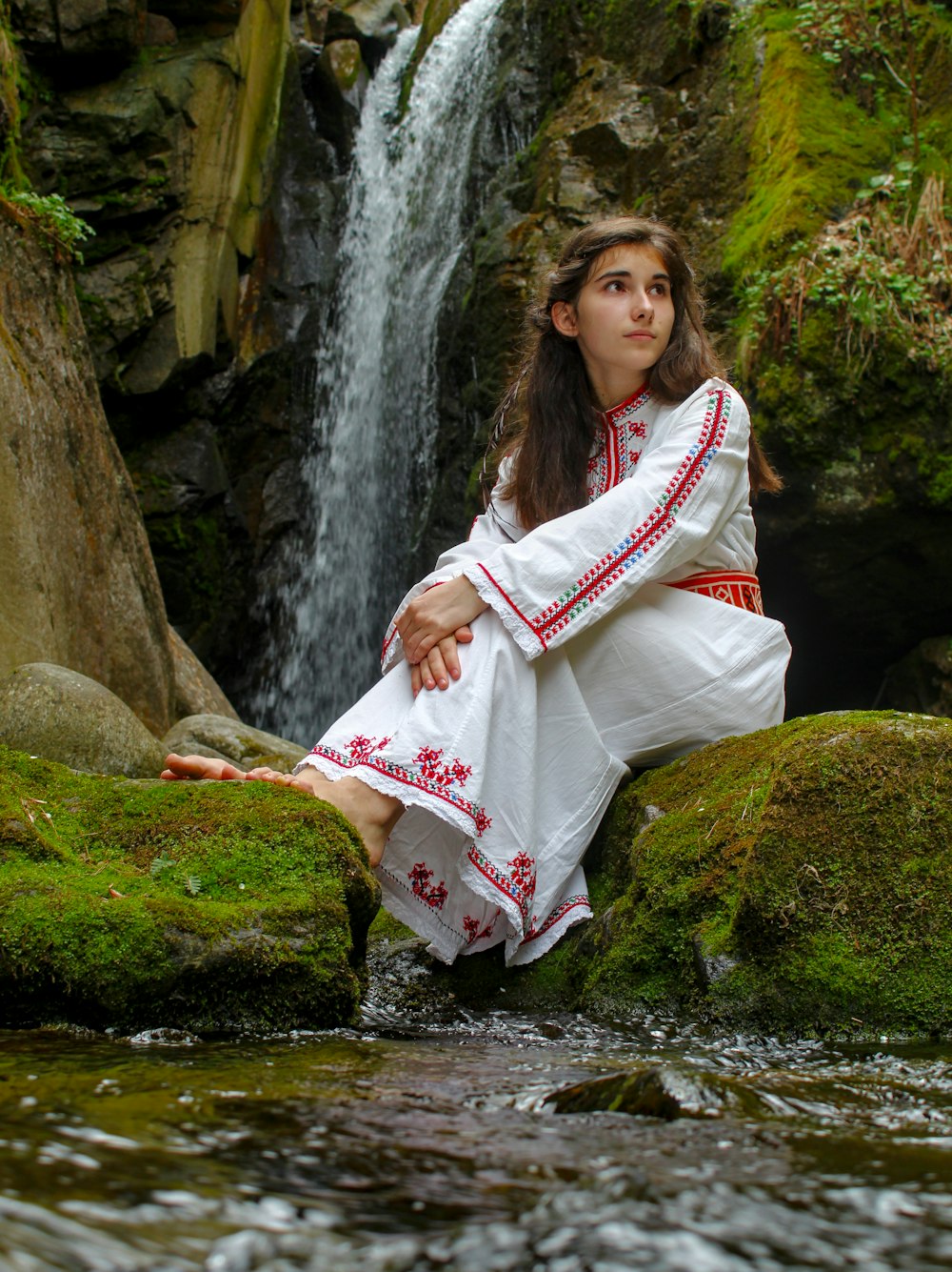woman in white and red dress standing on rock near river during daytime