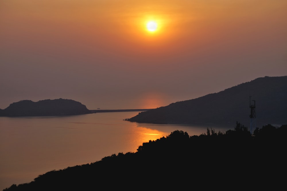 silhouette of mountain near body of water during sunset