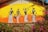 A vibrant mural depicts four stylized figures dressed in traditional clothing and adorned with jewelry. The art uses black and white against a bright orange and yellow gradient background. Nearby, colorful pink and purple flowers add to the scene, along with green foliage in the foreground.