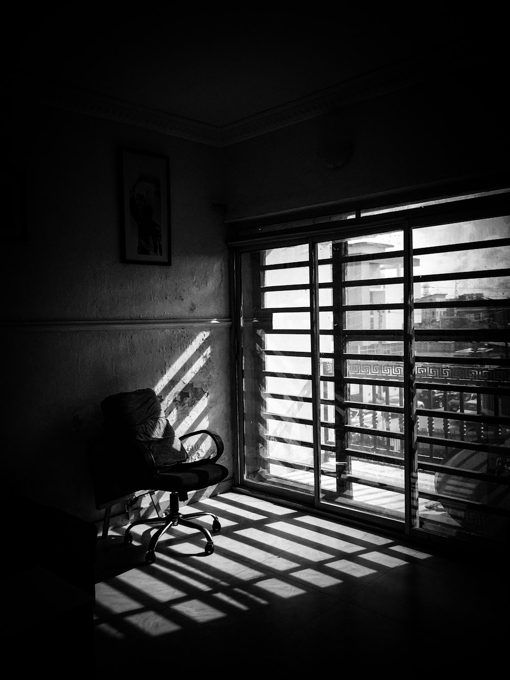 grayscale photo of black rolling chair near window
