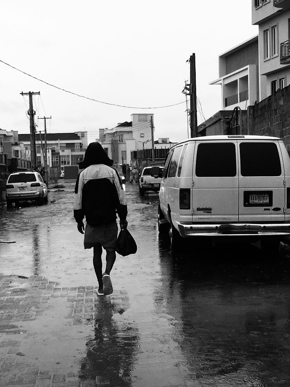 grayscale photo of man in black jacket walking on sidewalk