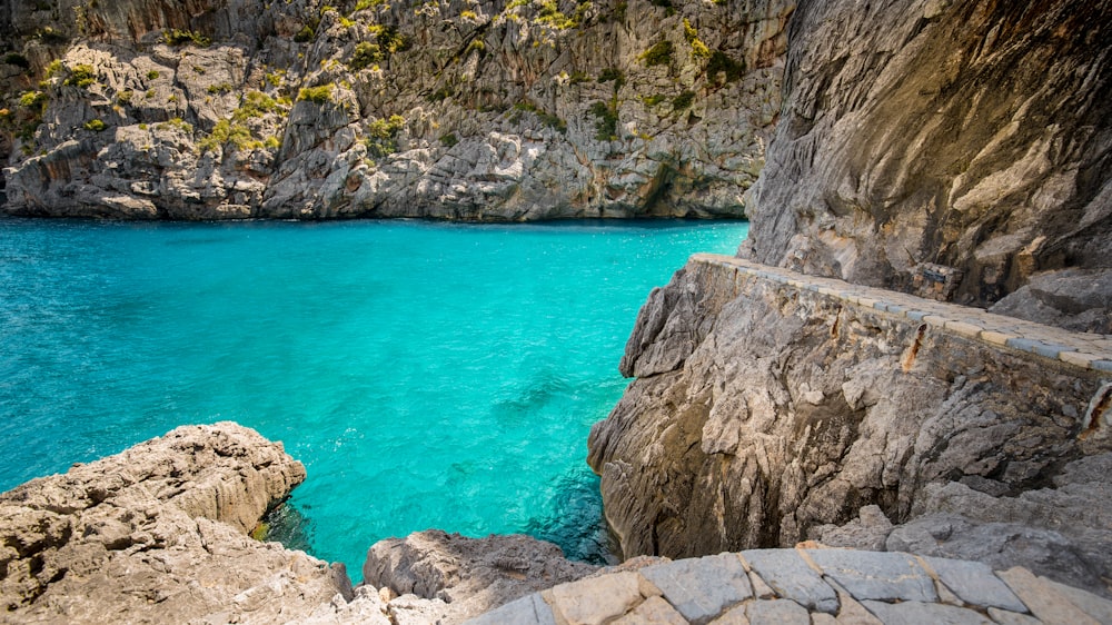 blue body of water between gray rocky mountain during daytime