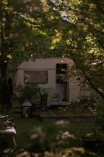 white and green rv trailer under green tree during daytime