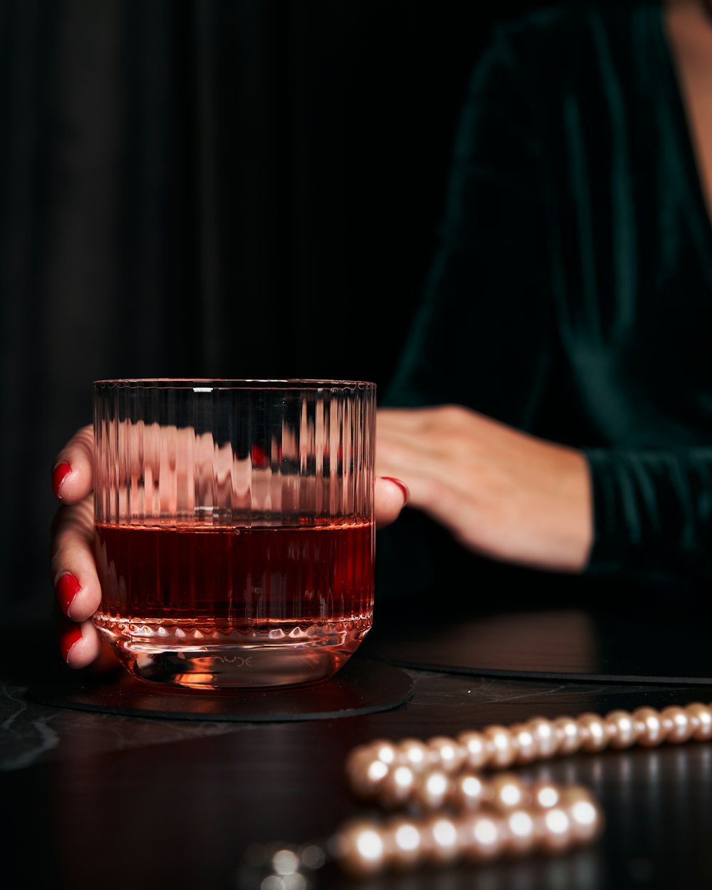 personne tenant un verre à boire transparent avec un liquide rouge