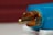 A close-up view of a metal audio or video plug, partially inserted in a blue housing with a golden metal tip and surround. The background is out of focus, featuring a maroon color.