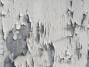 A wooden house facade with peeling paint being sodablasted, revealing fresh wood underneath.