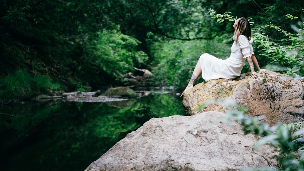 woman in white dress sitting on rock near river during daytime