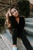 woman in black long sleeve shirt and blue denim jeans sitting on gray concrete stairs