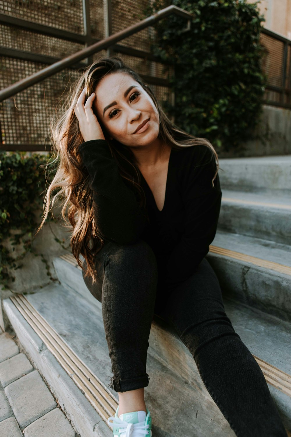 woman in black long sleeve shirt and blue denim jeans sitting on gray concrete stairs