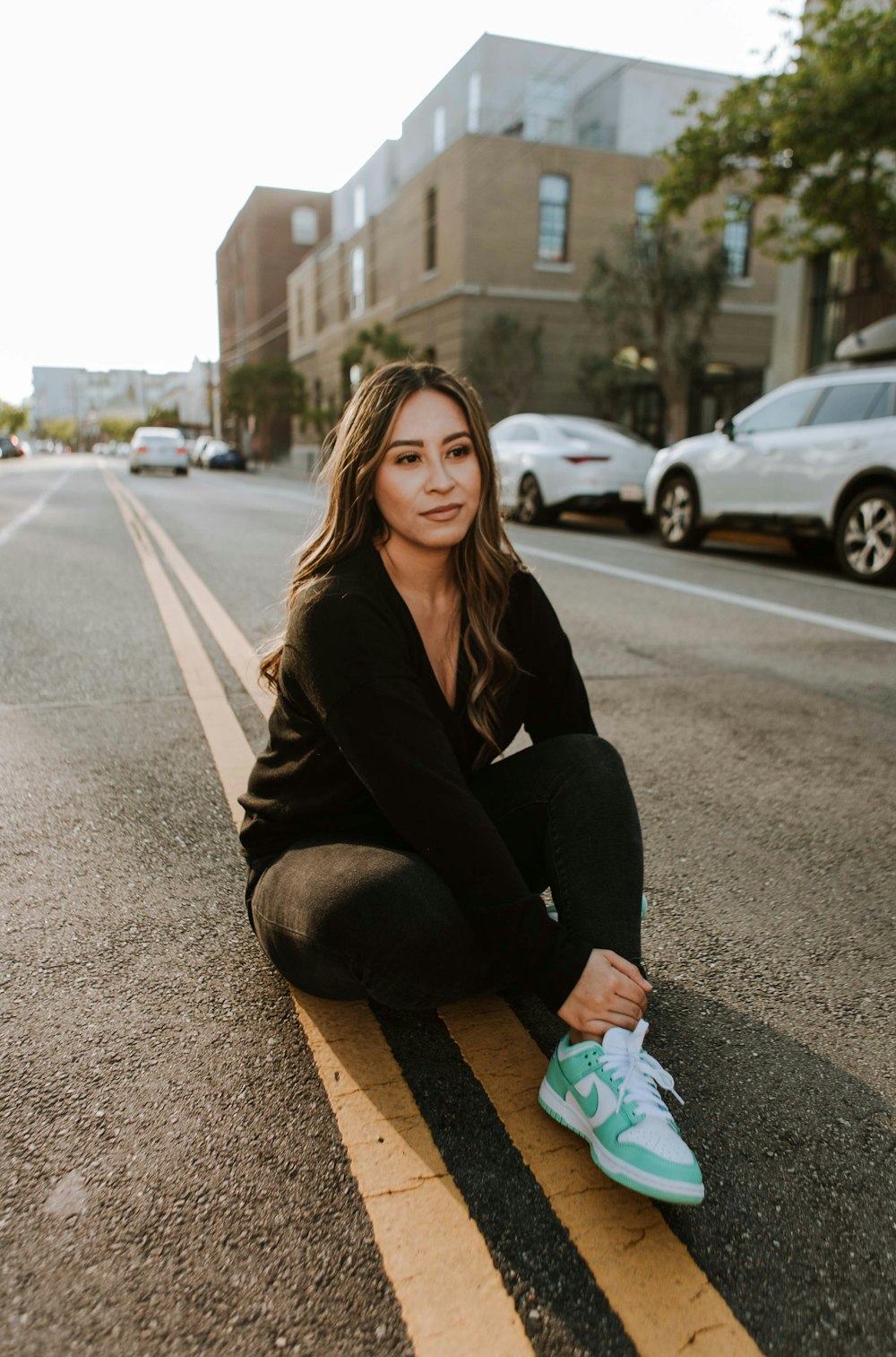 woman in black long sleeve shirt and black pants sitting on gray asphalt road during daytime