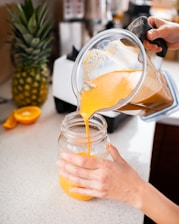 Close-up of hands preparing a smoothie with fresh fruits and greens.