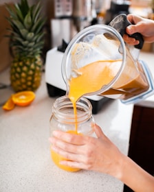 Close-up of hands preparing a smoothie with fresh fruits and greens.