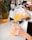Hands are pouring a bright orange blended beverage from a blender into a glass jar. A whole pineapple and a sliced orange are visible on a kitchen counter in the background.