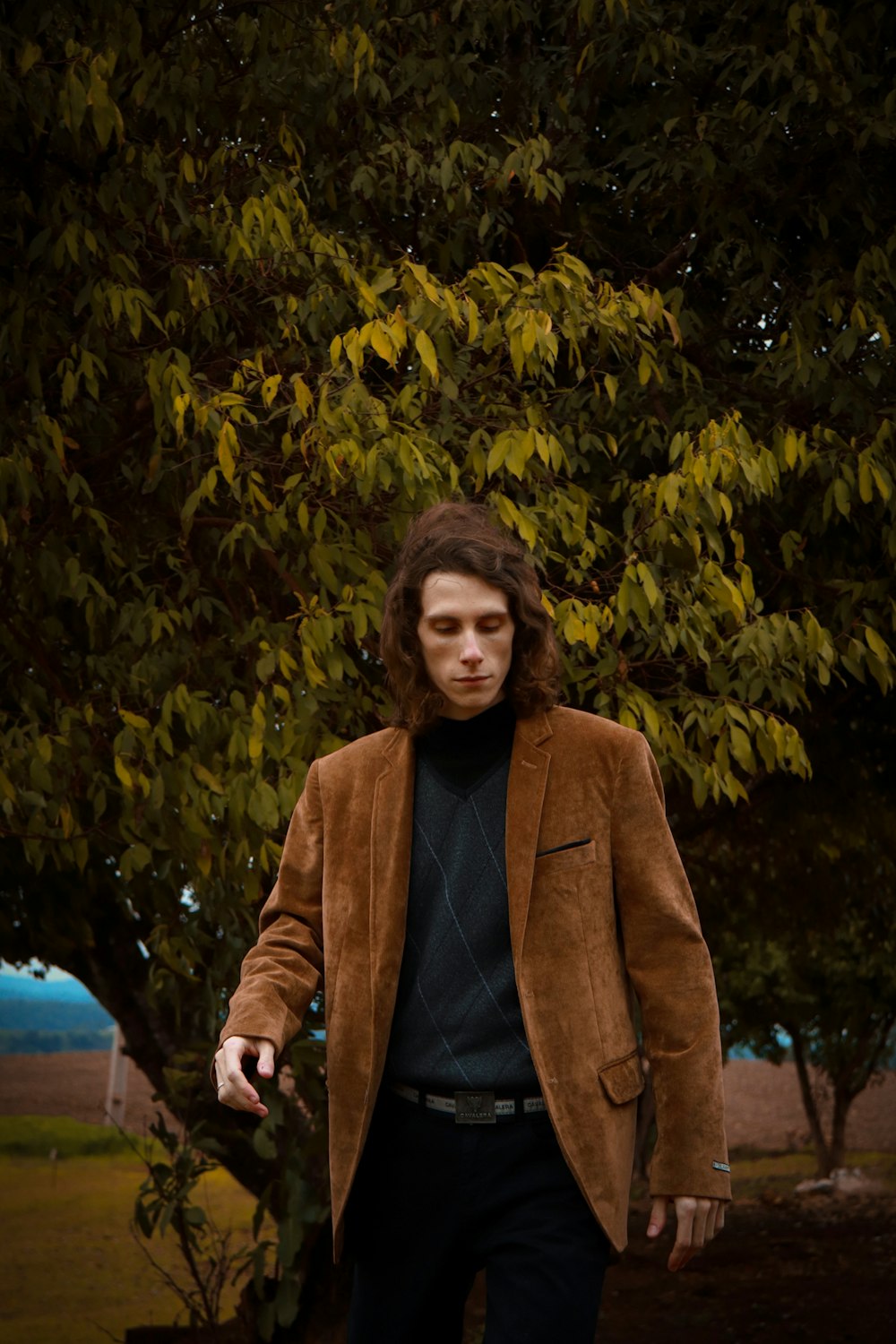 woman in brown coat standing near green tree during daytime