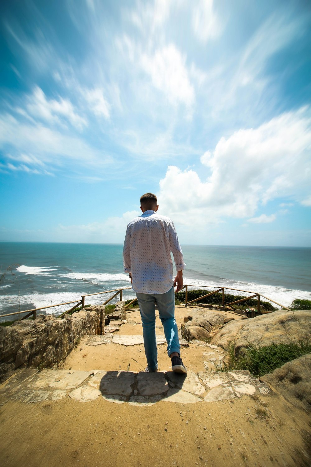 man in white dress shirt standing on brown rock formation near body of water during daytime