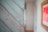 Weathered wooden boards with a light blue or teal paint are seen on the left, showcasing a rustic texture with visible knots and imperfections. On the right, there is a blurred interior with warm tones, featuring a framed artwork that's mostly red in color.