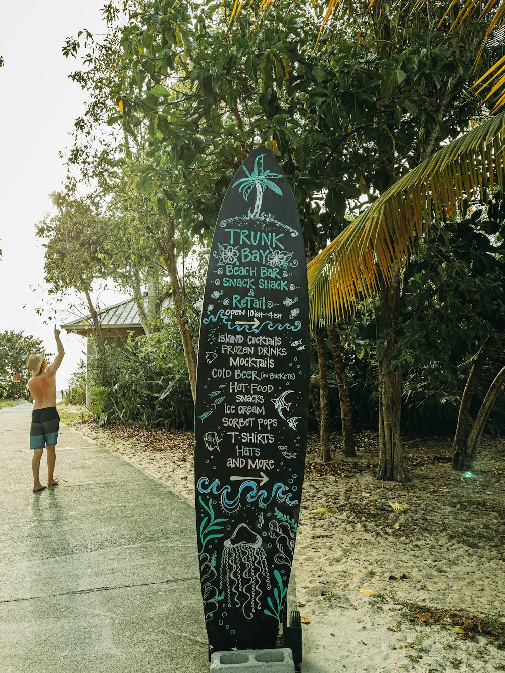 woman in black tank top and black shorts standing beside green and white surfboard