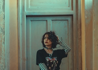 woman in black and white long sleeve shirt and black pants standing beside brown wooden door