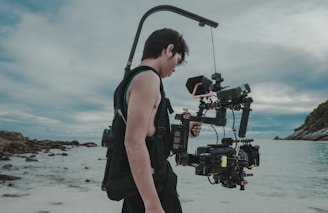 man in black tank top and black shorts holding black dslr camera standing on beach during