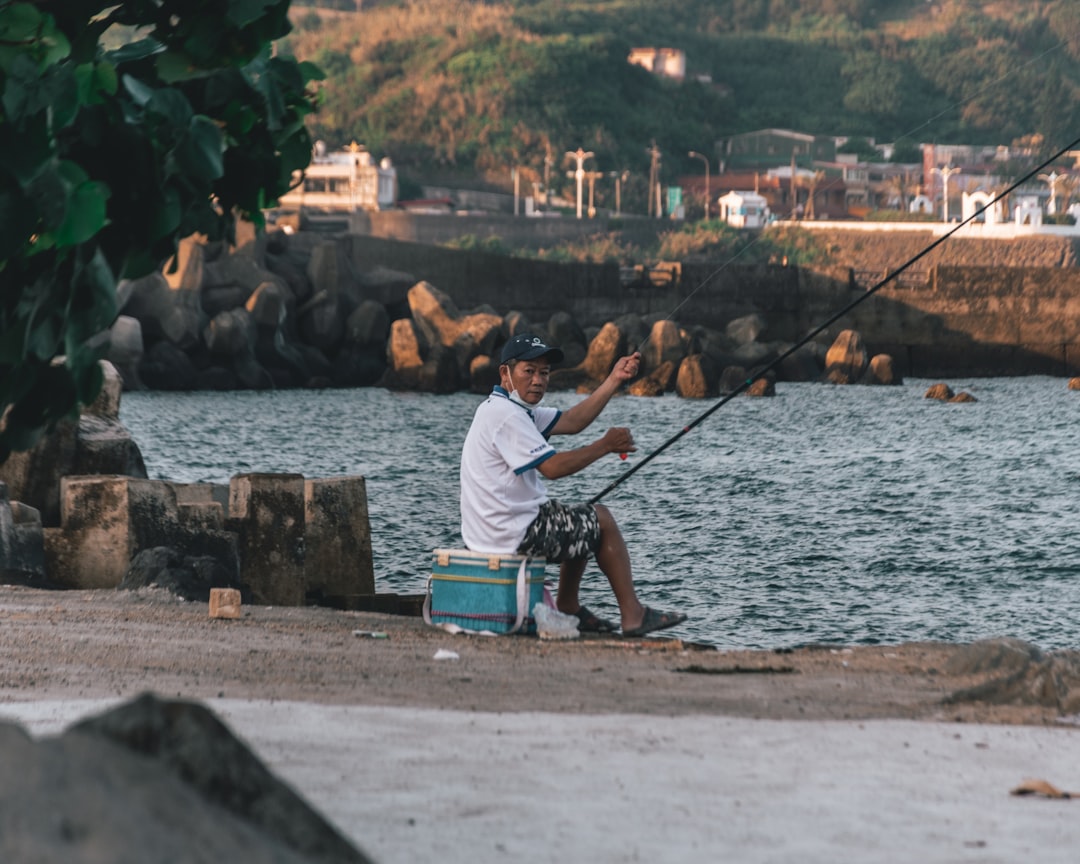 man in white t-shirt sitting on blue and black fishing rod during daytime