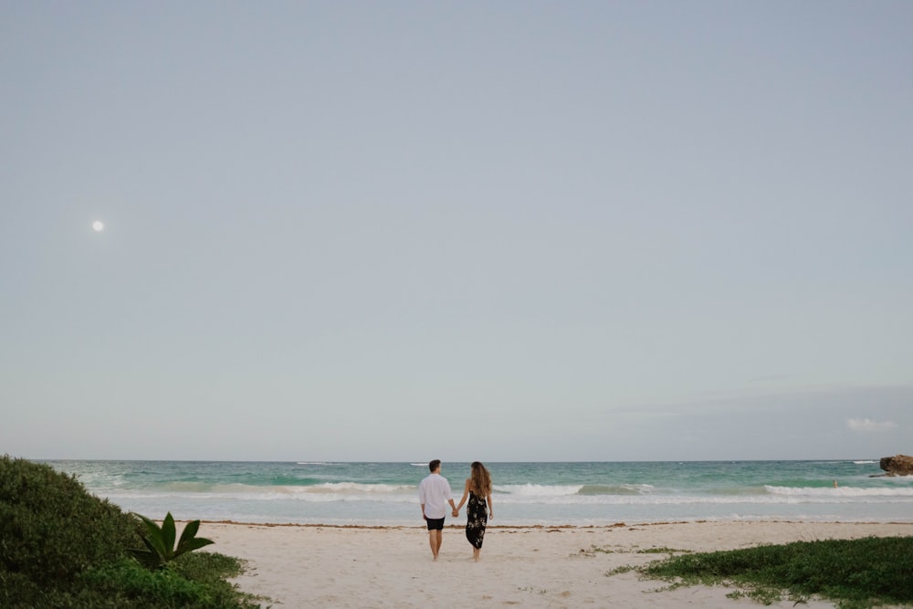 흰색 셔츠와 검은 반바지를 입은 여자가 낮 동안 해변을 걷고 있다