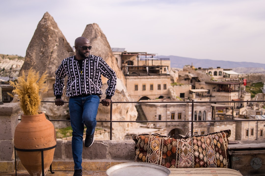 man in black and white long sleeve shirt and blue denim jeans standing near brown concrete