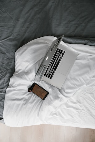 macbook pro beside brown leather wallet on white bed