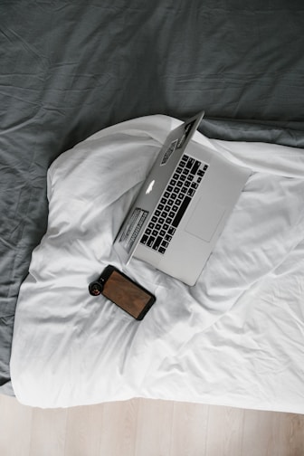 macbook pro beside brown leather wallet on white bed