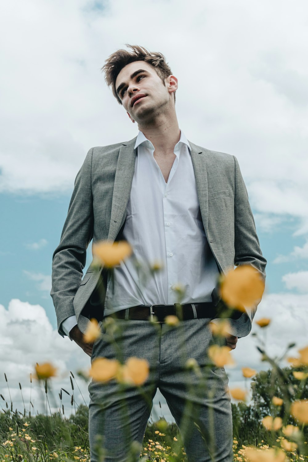 man in grey suit jacket standing on yellow flower field during daytime